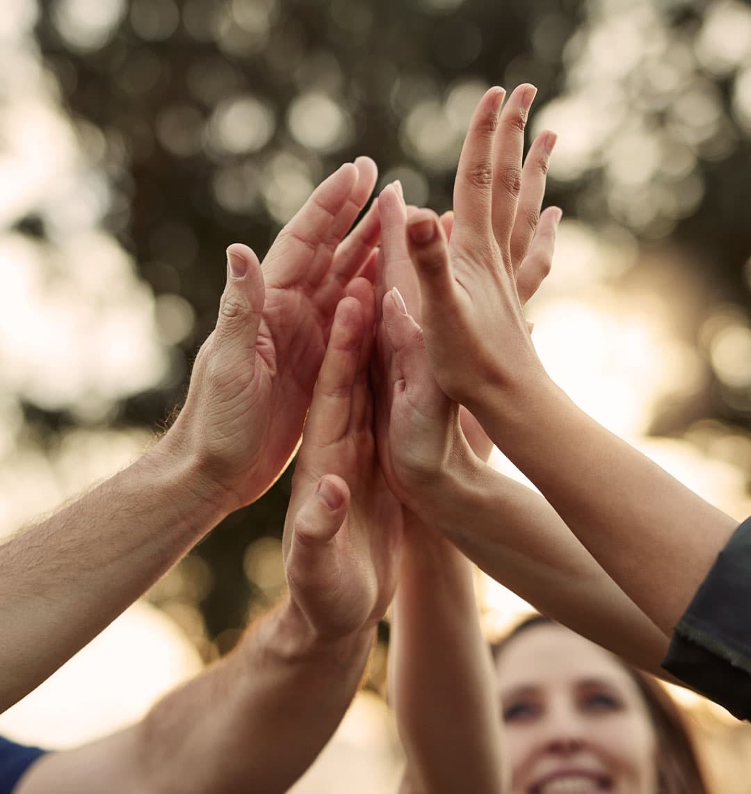 In der Mitte des Bildes treffen sich einige Hände zu einem gemeinschaftlichen High-Five.