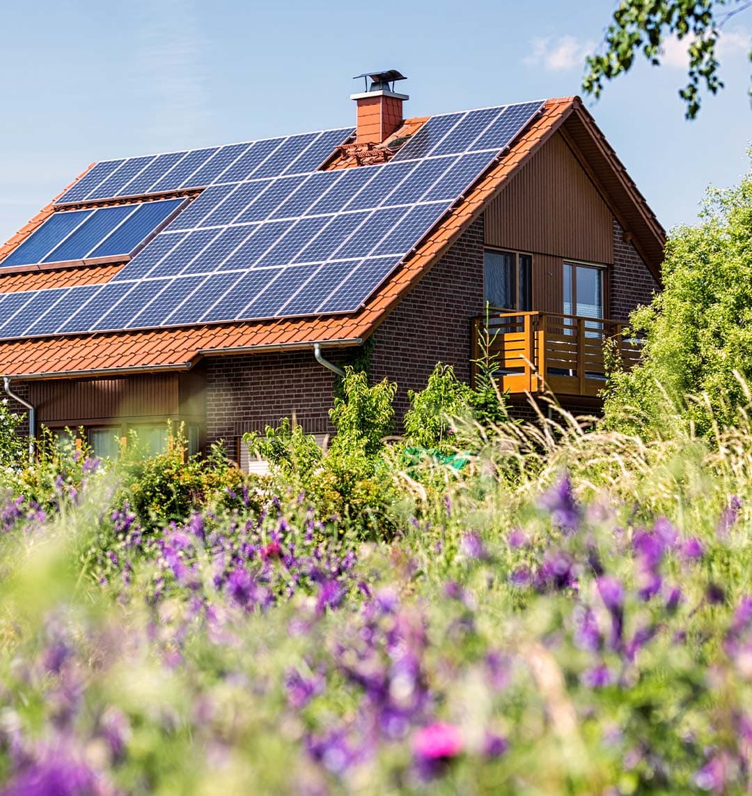 Auf dem Bild befindet sich ein Haus in einem grünen Garten. Auf dem Dach des Hauses sind Solarpanele angebracht.