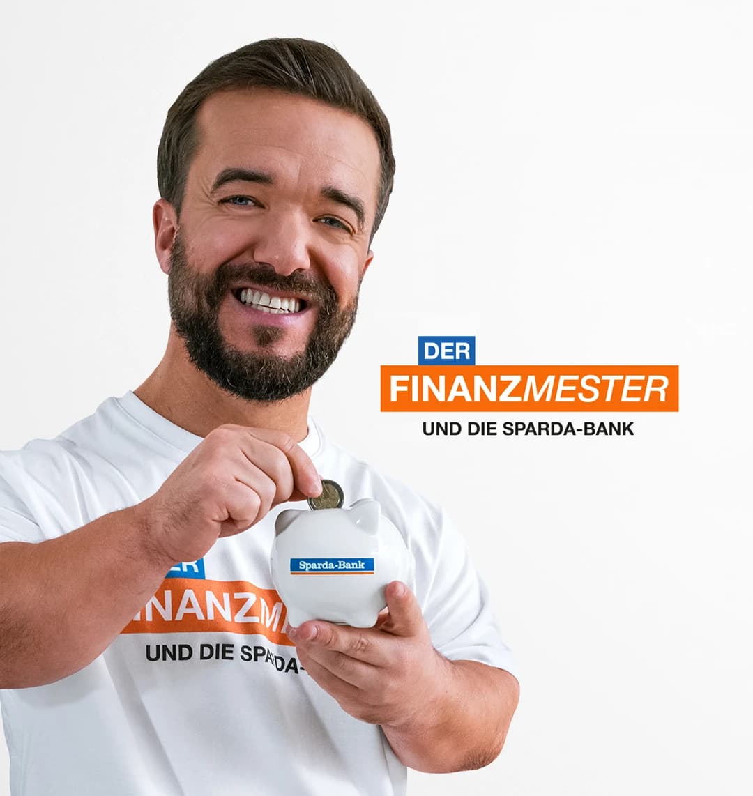 Ein lächelnder Mathias Mester steckt eine Münze in ein Sparschwein mit Sparda-Bank-Logo und trägt ein T-Shirt mit „DER FINANZMESTER UND DIE SPARDA-BANK“