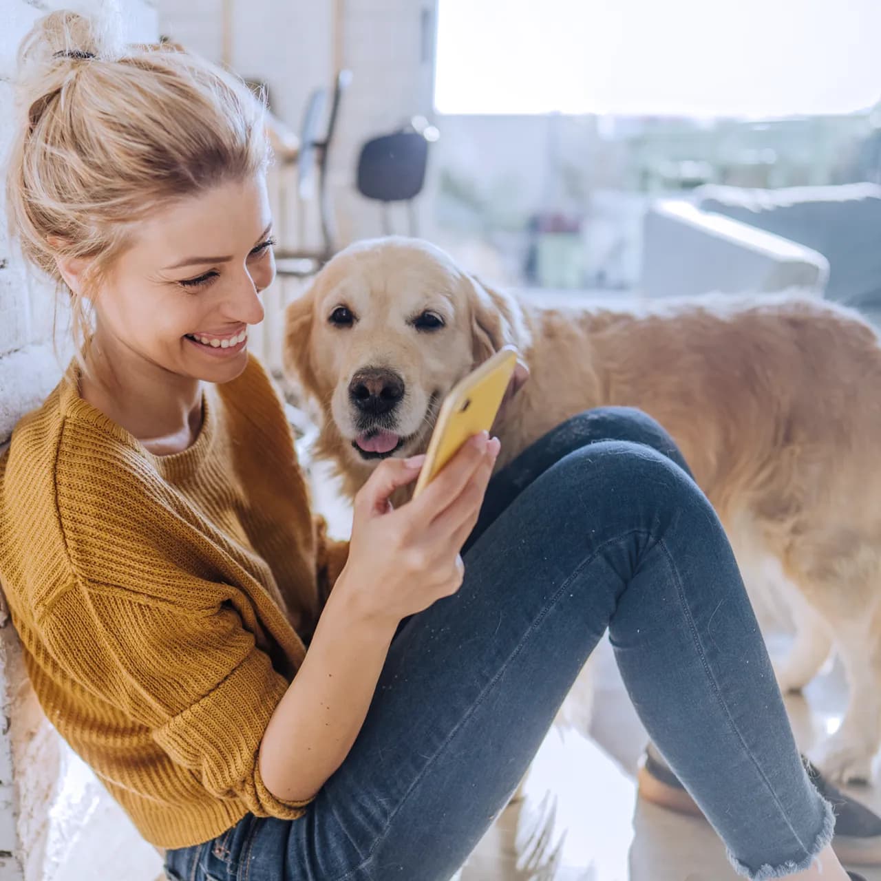 Lächelnde Frau mit Smartphone neben einem Golden Retriever.