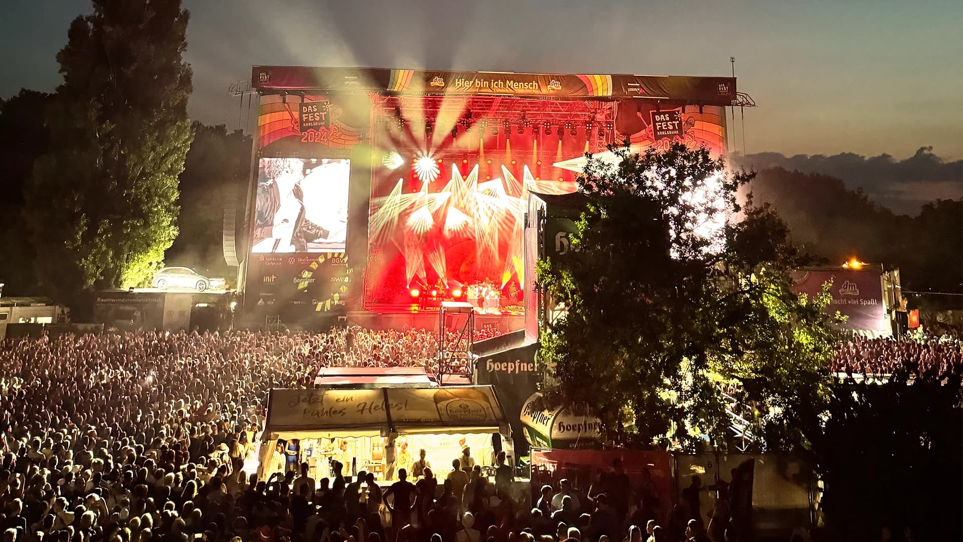 Vor der Hauptbühne von das Fest stehen viele Menschen. Die Lichter der Bühne erhellen die Menge und die dunkle Umgebung.